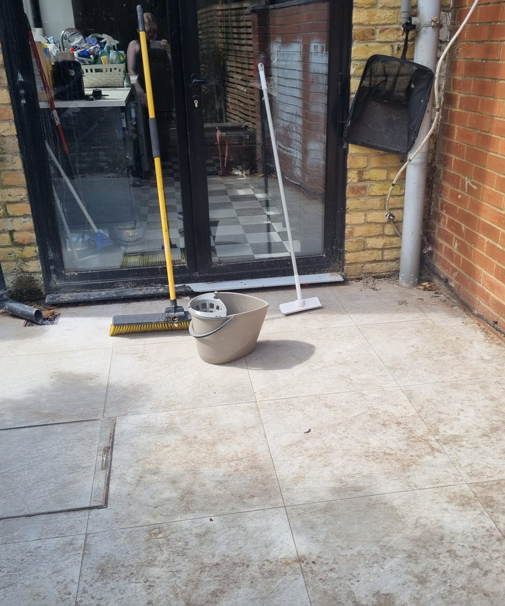 A grimy patio with two brooms and bucket ready to clean