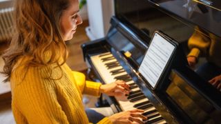 Woman sits at piano with sheet music on a tablet