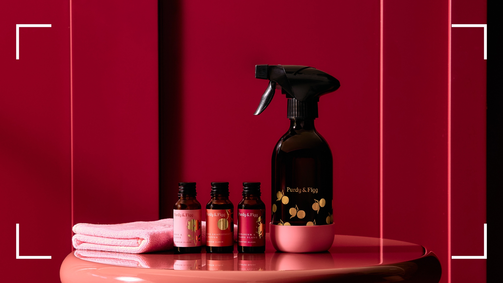 The spray, concentrates, base, and cloth in the Purdy &amp; Figg x CoppaFeel! displayed in a pink room