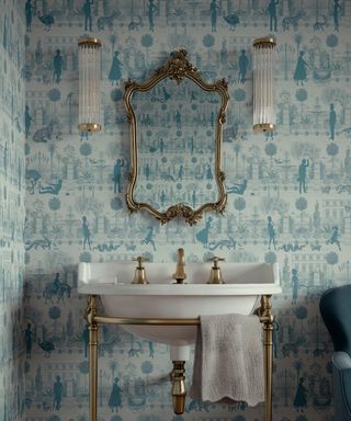 bathroom with blue green toile wallpaper, white sink, classic gilt mirror, gold style faucet, wall lights