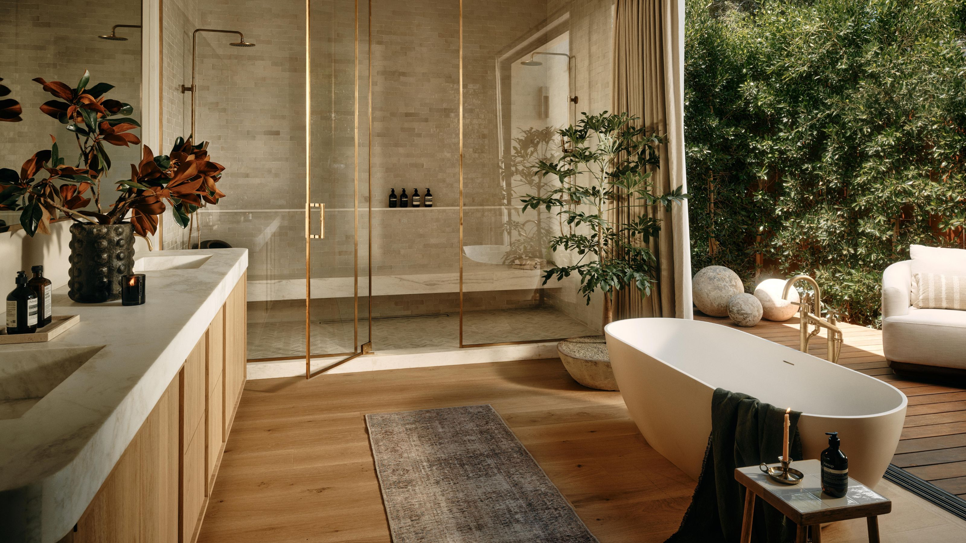 an organic modern primary bedroom with oak and marble vanity, freestanding tub beside doors out to a patio area