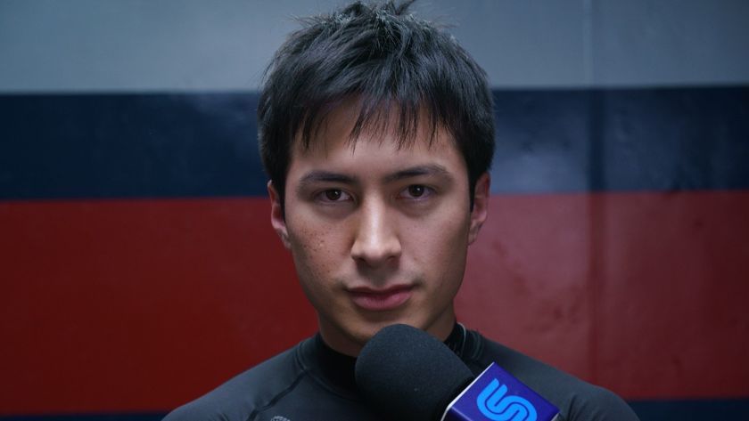 Hudson Williams looking into the camera while a mic is held up to his mouth in Heated Rivalry.