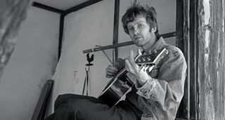 A black-and-white portrait of alt-country artist Greg Freeman playing an acoustic guitar