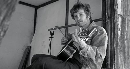 A black-and-white portrait of alt-country artist Greg Freeman playing an acoustic guitar