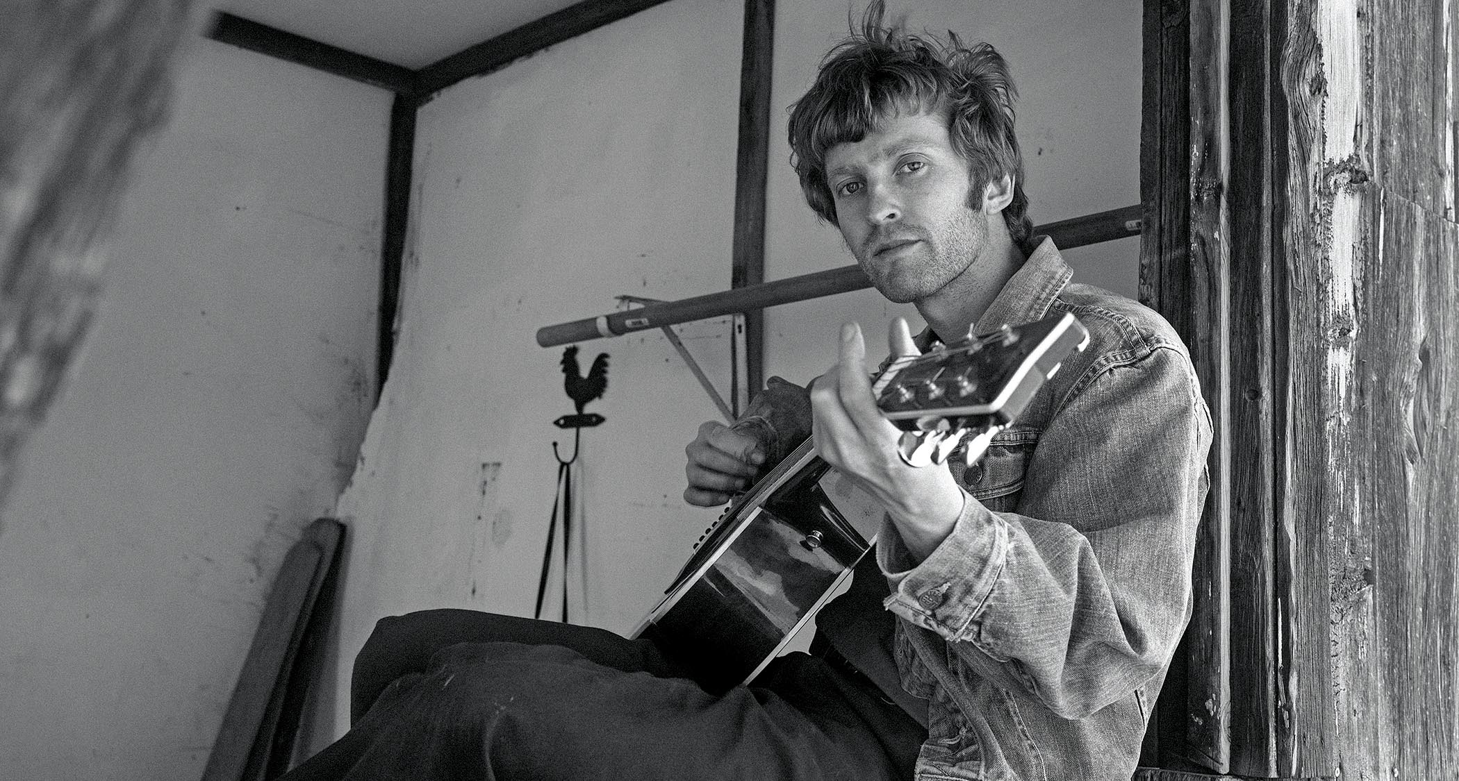 A black-and-white portrait of alt-country artist Greg Freeman playing an acoustic guitar