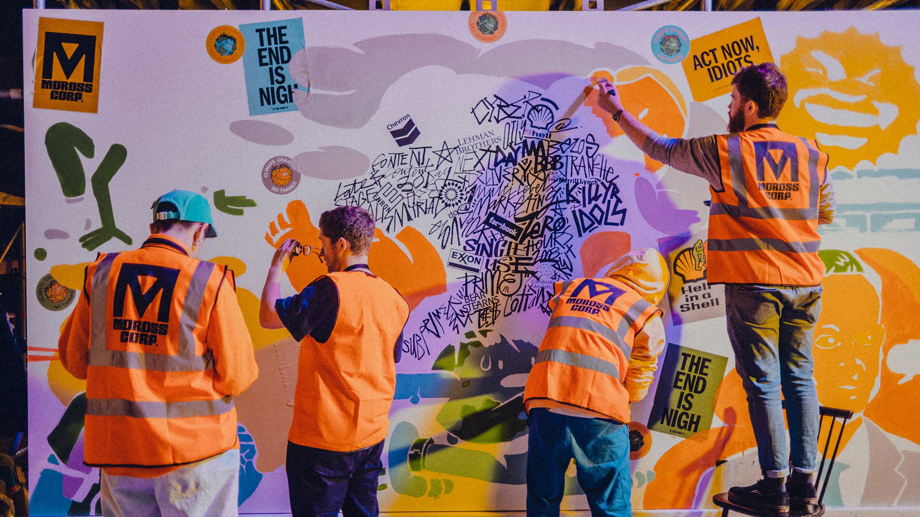 Four men in high visibility jackets assembling graffiti, art and bright stickers onto a large white board