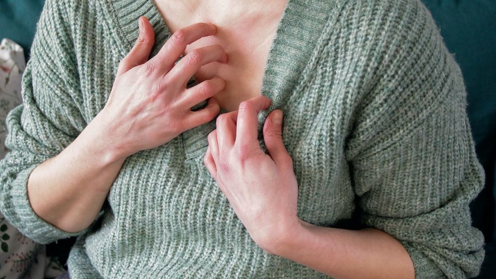 Woman in green sweater scratching chest.