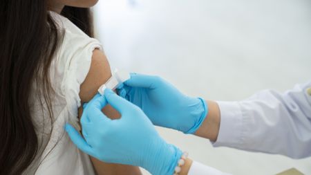 A healthcare worker places a bandage on a girls' arm after a vaccine