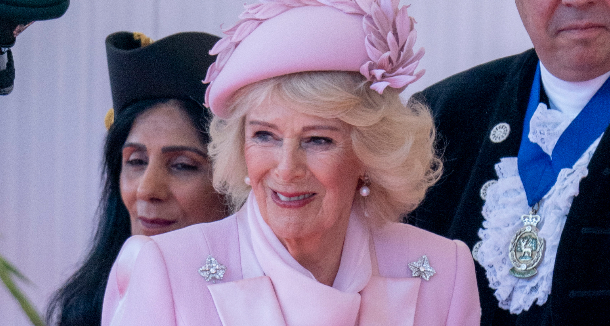 Queen Camilla in a pink hat and coat smiling