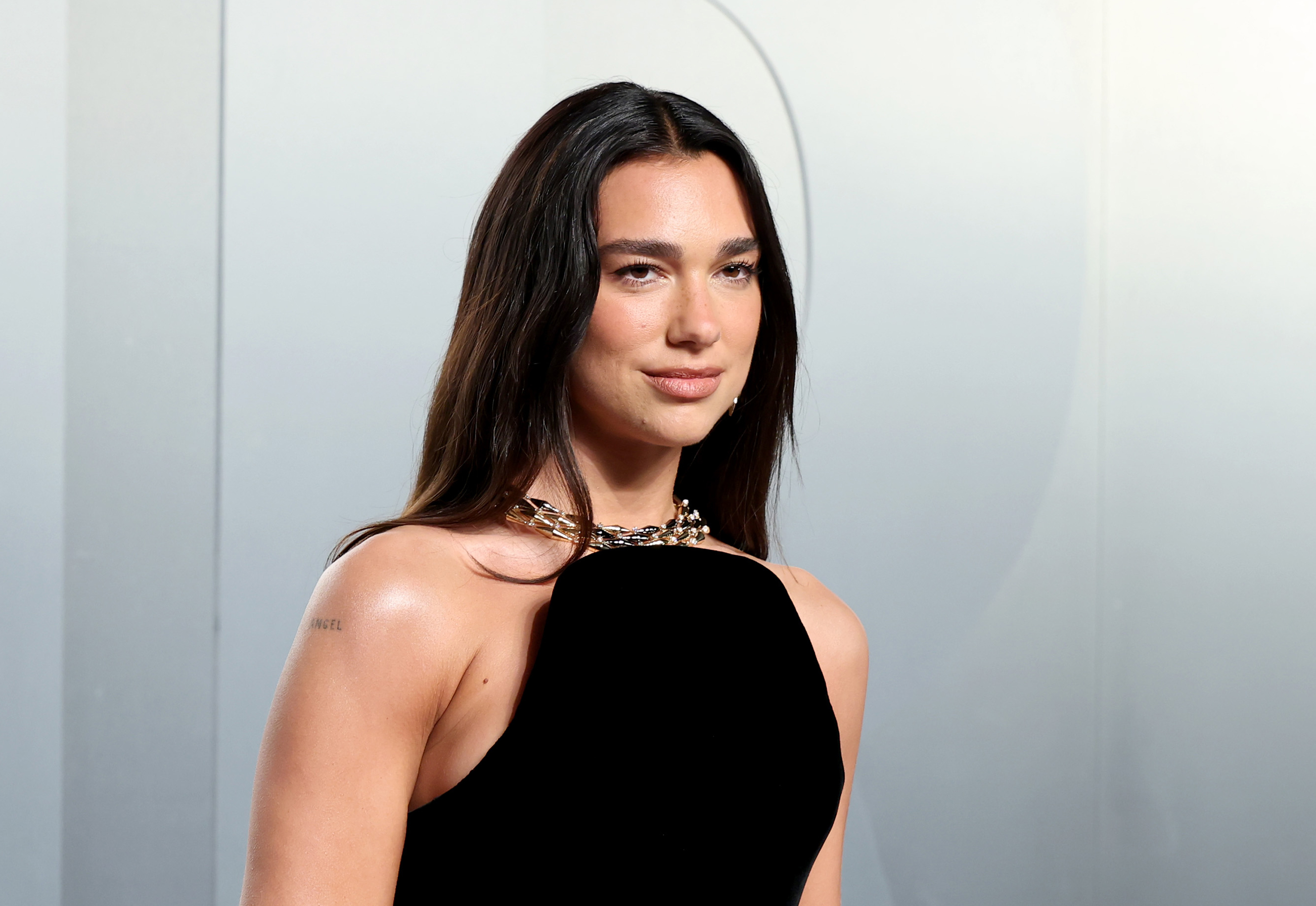 Dua Lipa wearing a black dress standing in front of a grey background