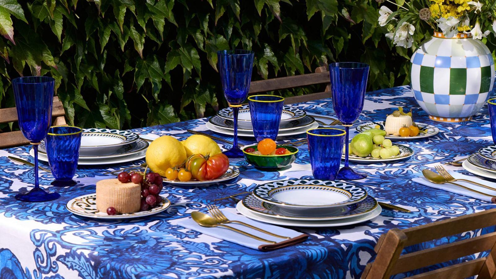 Tablescape with blue and white printed tablecloth, deep blue wine glasses, ble and white plates and a blue and green vase