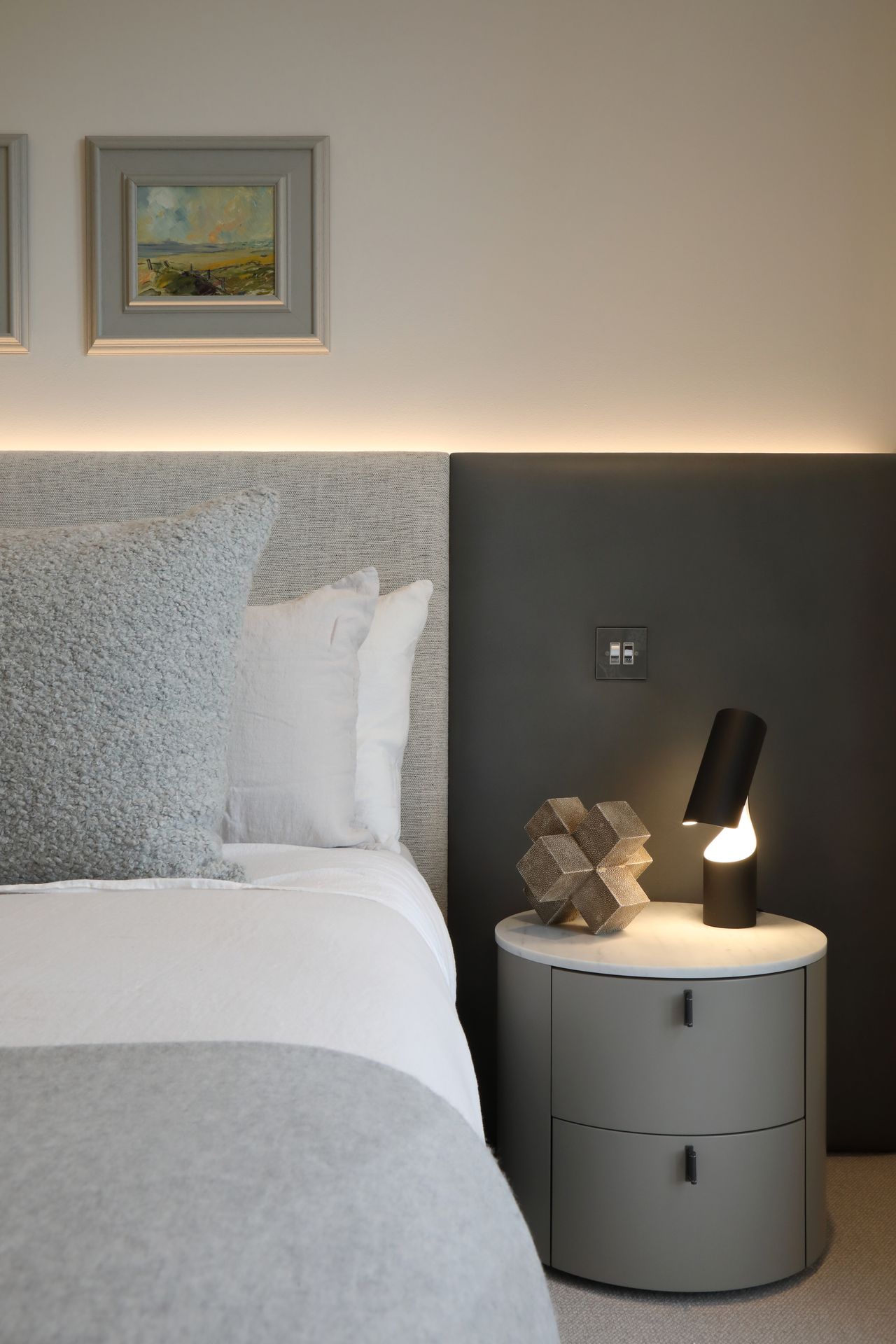A bedroom with grey bedding and a recessed light behind the bed