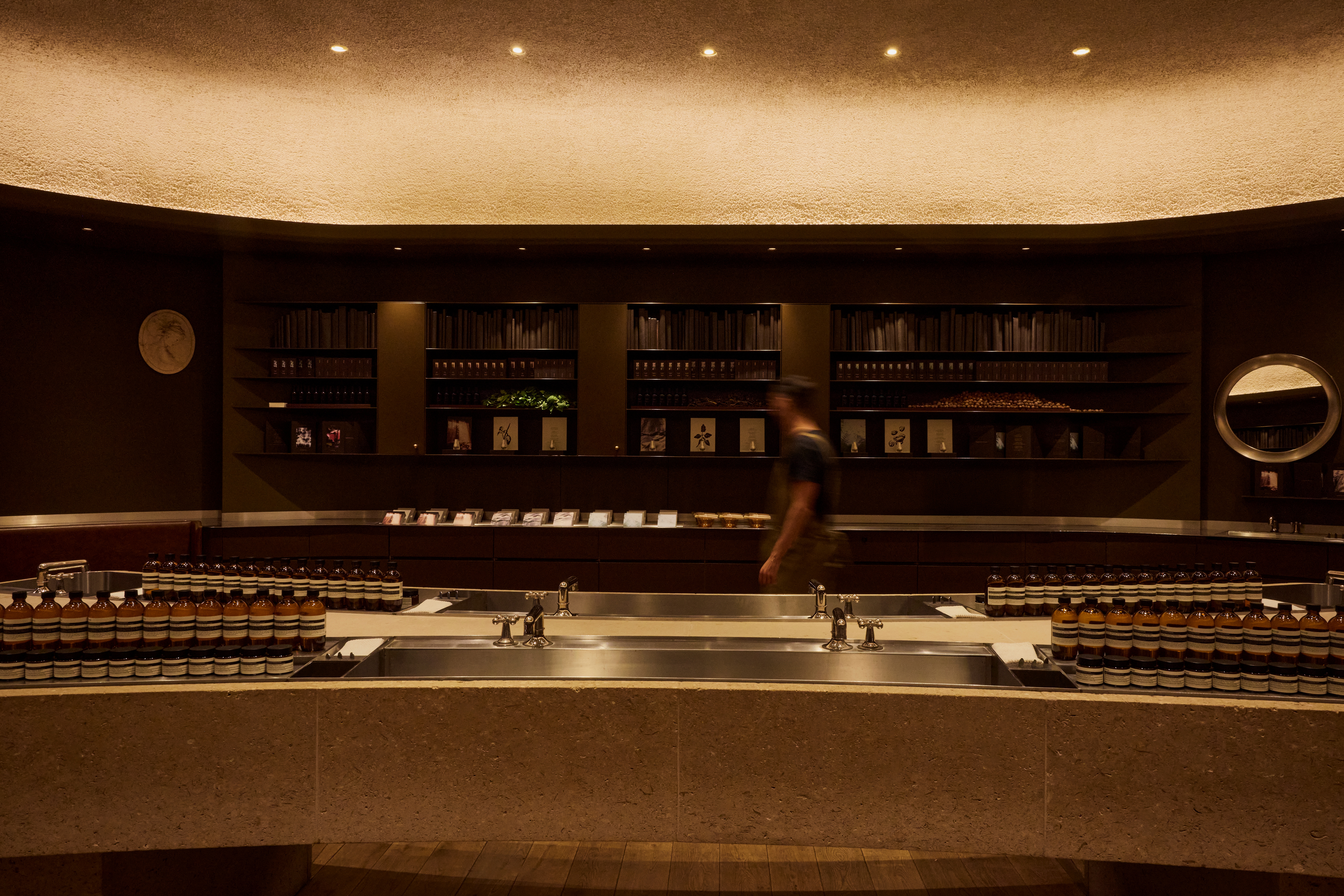 Interiors of a dimly lit, futuristically designed fragrance store with an illuminated roof, chocolatey interiors, and plenty of books and paper installations styled sophisitcatedly.