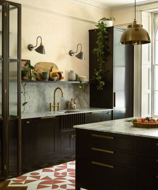 kitchen with dark units, swan necked metal wall lights with small metal shades on wall above sink and brass metal pendant shade above kitchen island