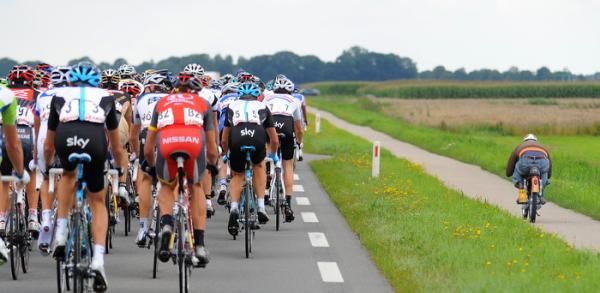 A man on a very small bike keeps pace with the peloton.