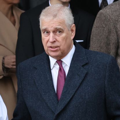 Prince Andrew wearing a blue coat and red tie looking skeptical