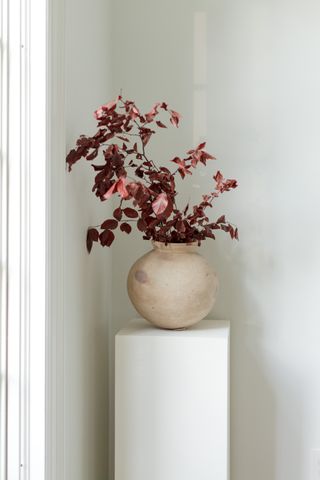 A ceramic vase on a white pedestal filled with stems of red leaves