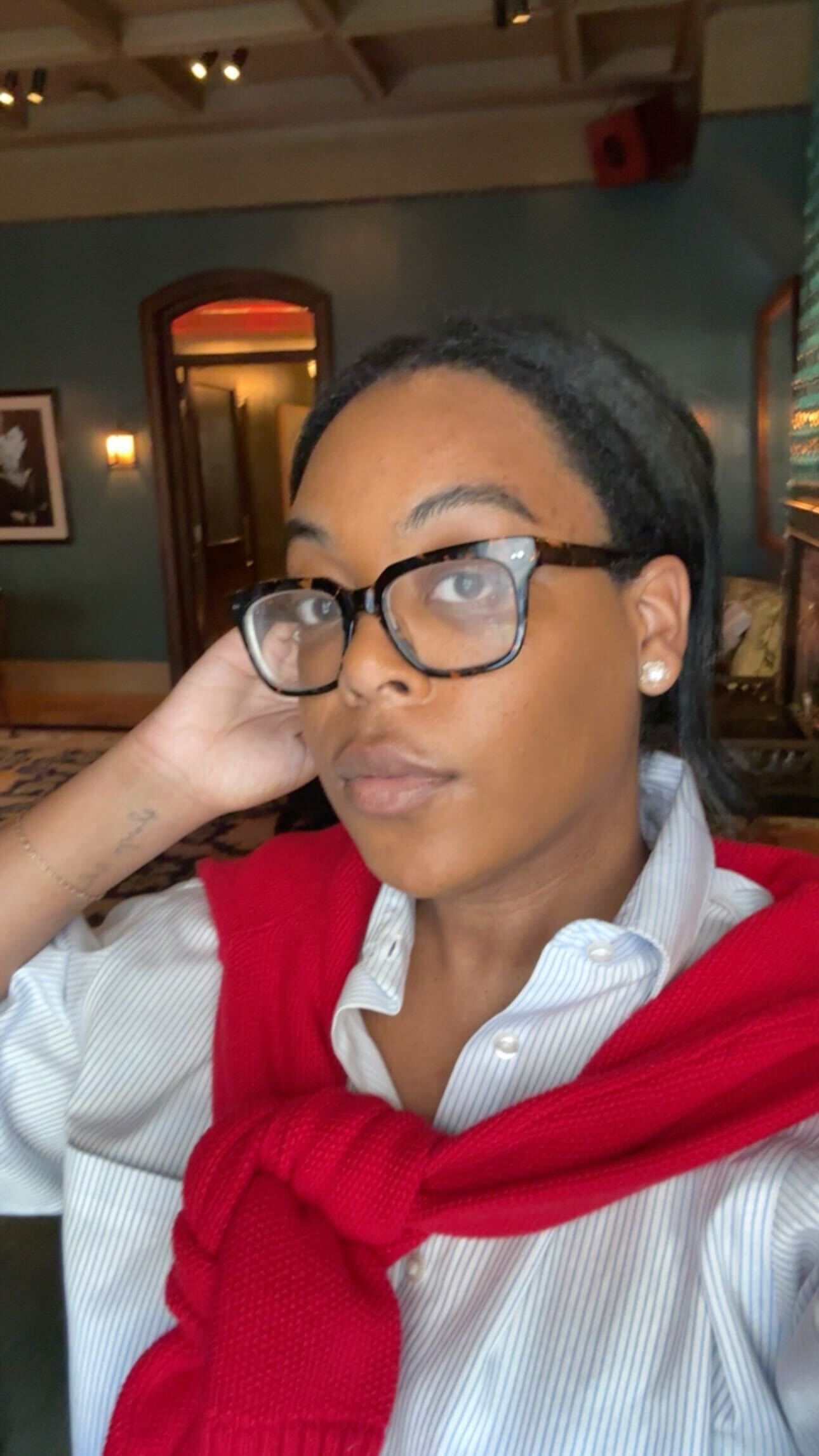 a woman with dark hair and glasses wearing a striped shirt and red sweater