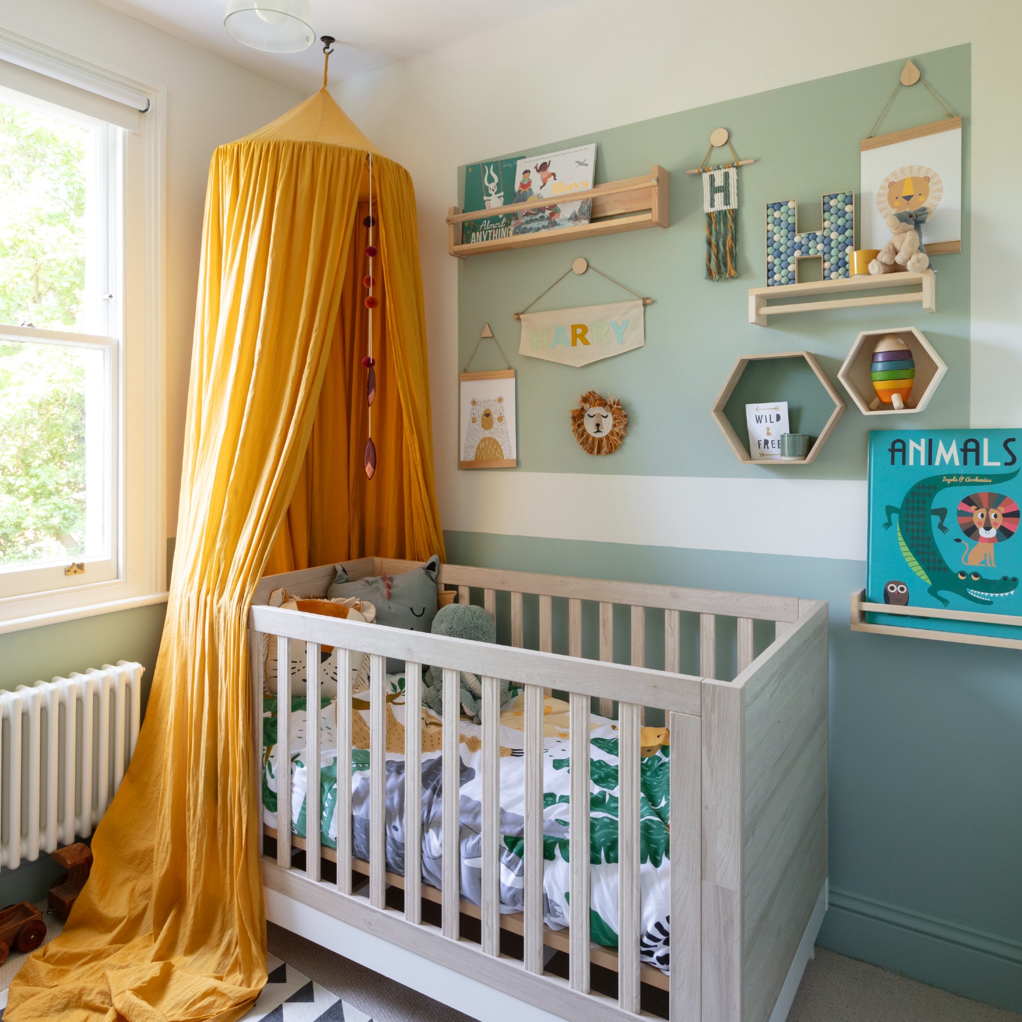 A jungle-themed nursery with green walls and a mustard yellow canopy over the cot