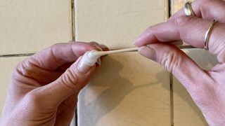 An earbud tip being dried with a cotton swab, on beige background