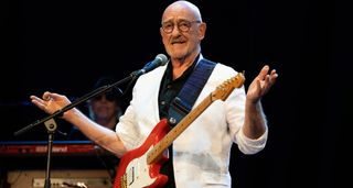 Dave Mason wears a white jacket and plays a red Strat onstage