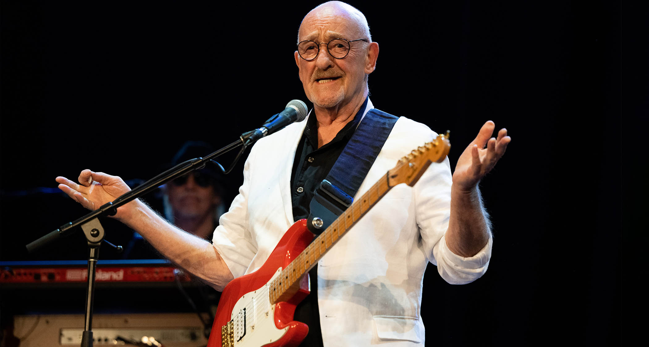 Dave Mason wears a white jacket and plays a red Strat onstage