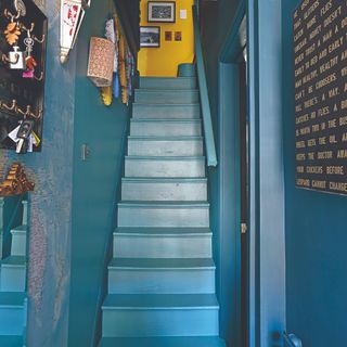 A blue-painted staircase with matching walls and a contrasting yellow wall on the landing