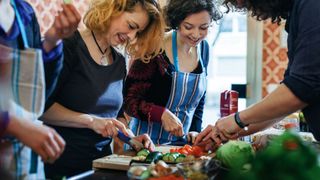 Women cutting up vegetables on a wooden chopping board