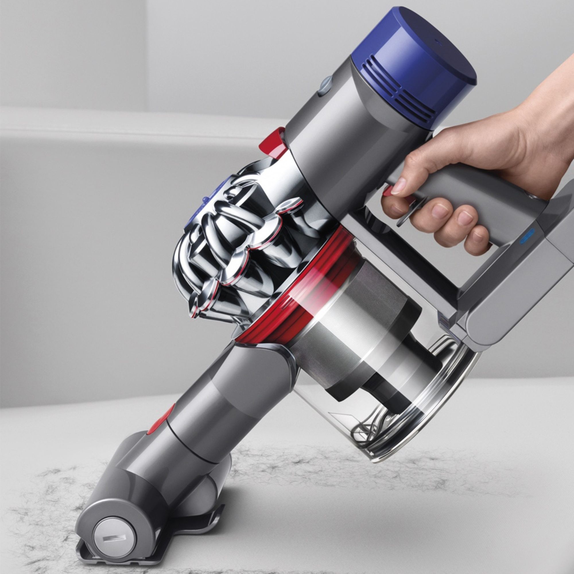 A hand holding the Dyson V8 over a white surface. 