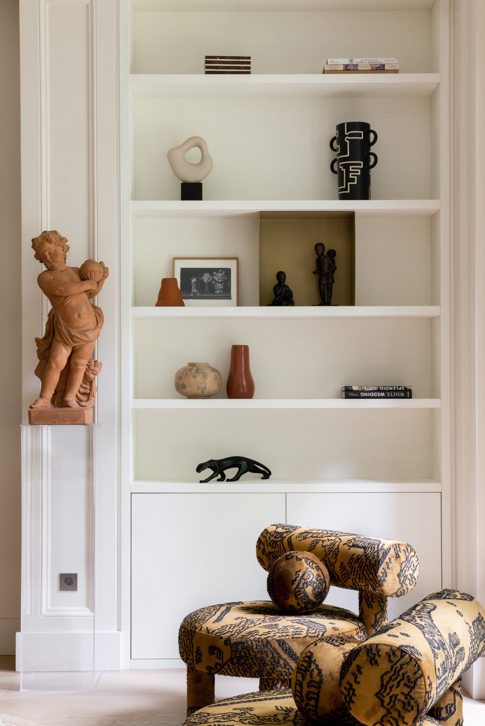 White floor-to-ceiling bookshelves with ceramic decor on them. There are two tiger-printed chairs in the front.