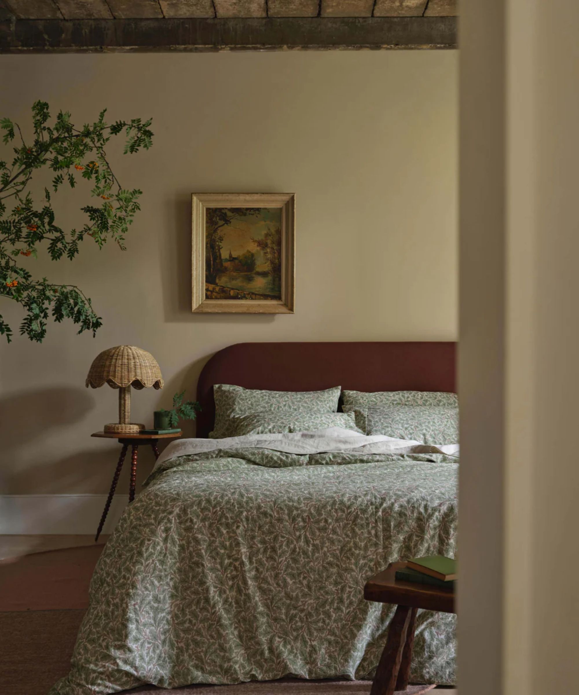Rustic bedroom with brown headboard, green and white botanical bedding, rattan lamp on wooden bedside table