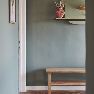 Hallway with light sage green paint and wooden bench.