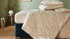 Woolroom comforters and pillows on a mattress against green walls.