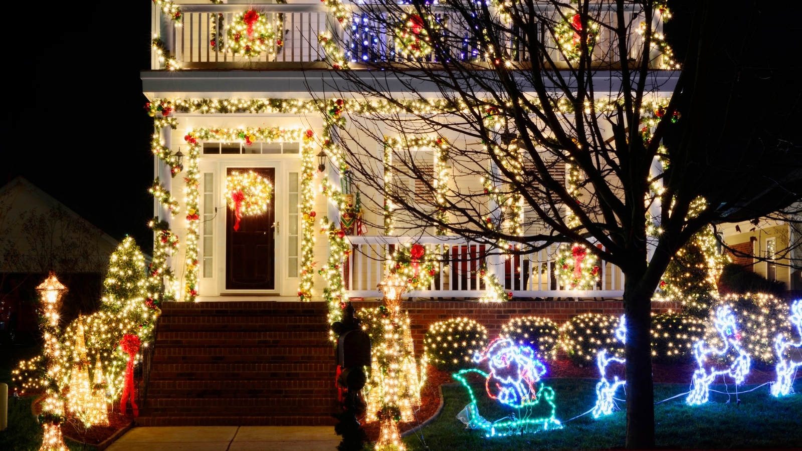 Shot of home exterior with bright, multi-colored Christmas lights, against nighttime background.