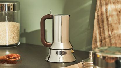 an One of the best moka pots on the market, the Alessi 9090 moka pot on a countertop next to a spoon of ground coffee