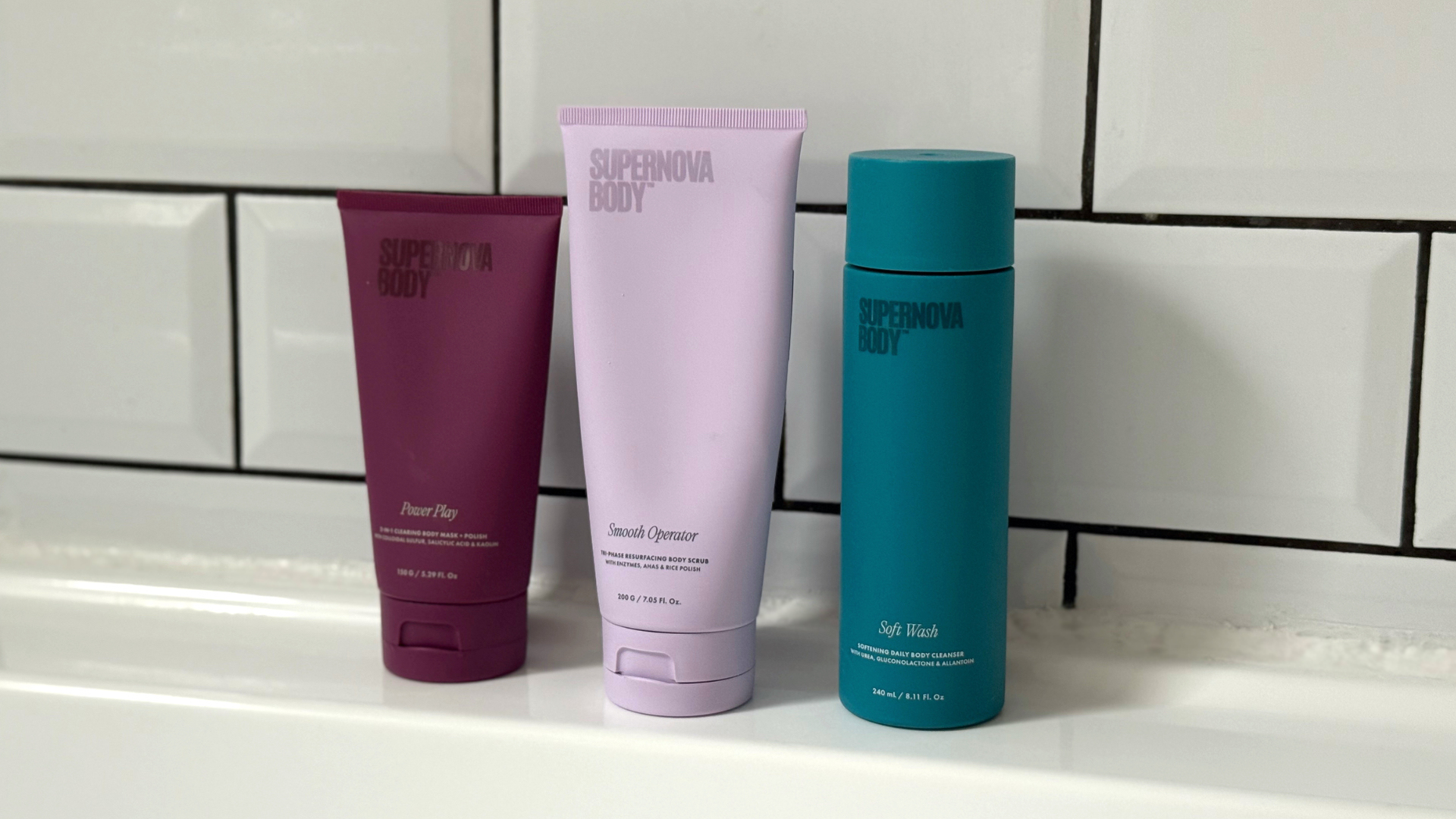 Close up of the three Supernova Body products stood on the side of a white bathtub in front of a white tiled background 
