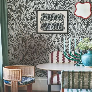 A dining room with walls covered in a graphic wallpaper and mismatched seating covered in patterned upholstery