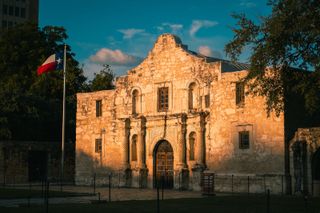 The Alamo at sunrise with the Texas flag waving.