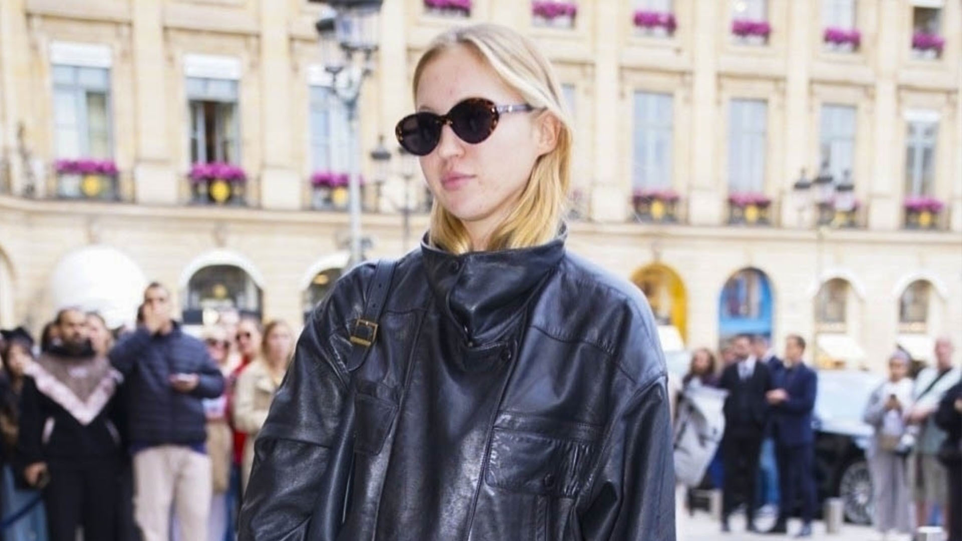 Lila Moss wearing a black leather jacket, gray flared pants, and black boots