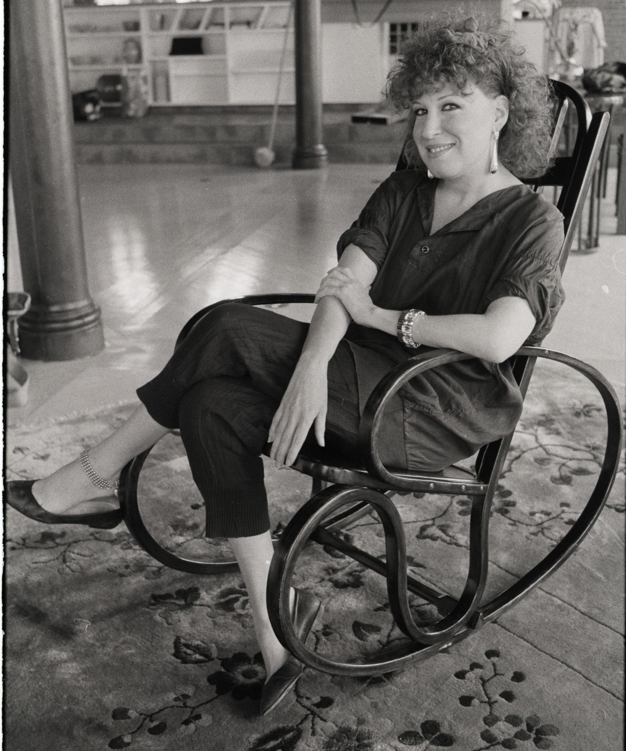 bette midler in a rocking chair in her living room