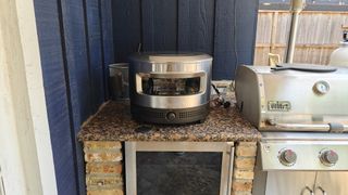 The Solo Stove Pi Prime sitting on a back porch counter next to a grill