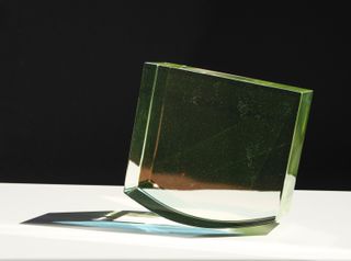 green tinted glass sculpture in parallelepiped shape balancing on a curved side