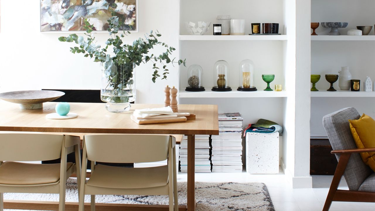 A dining table with a vase in the centre and minimalist shelves in the background