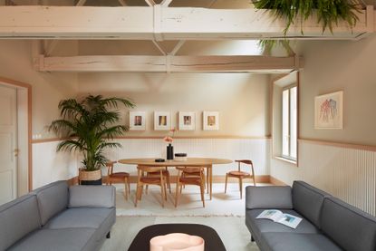 Living room with two grey couches, a black coffee table, a dinning table and chairs, a potted plant, a white rug and a potted plant.