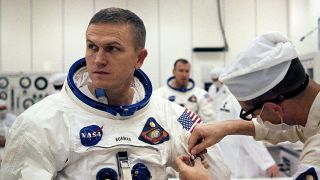 technicians help an astronaut get into a spacesuit