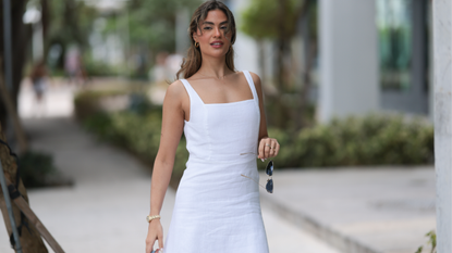 Jessica De Oliveira seen wearing gold earrings, Riani white strappy long dress, Jacquemus light blue suede leather Bambino Long bag, Dior gold cat-eye sunglasses, on December 09, 2023 in Miami, Florida. 