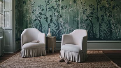 dark leafy green wallpaper in a sitting room with two cream armchairs