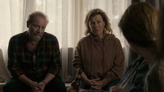 Peter Mullan in a dark top as Phil and Robyn Malcolm in a brown top as Penny sit next to each other in After The Party.