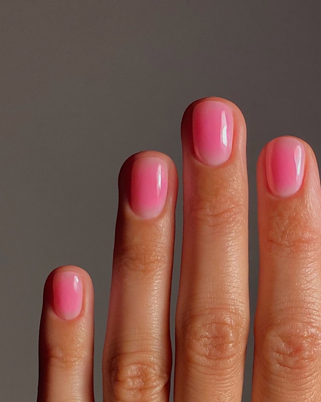 Short, square nails with a sheer pink base and bright pink aura centers, finished with a glossy topcoat