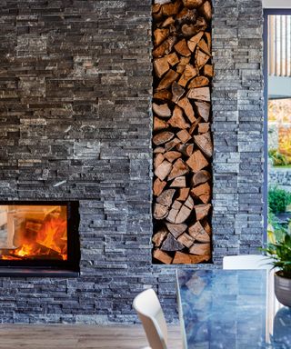 A cut out section of a statement wall filled with logs next to a clear glass fireplace